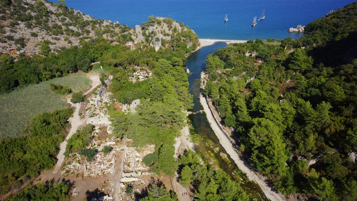 Ruins of ancient Olympos emerging from dense vegetation near the Mediterranean shore